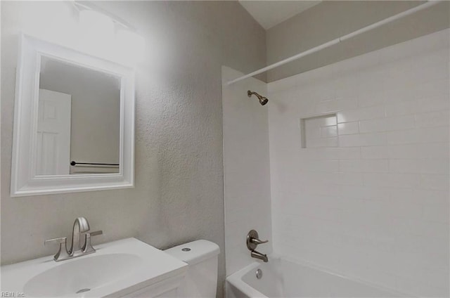 bathroom featuring a textured wall, tub / shower combination, vanity, and toilet