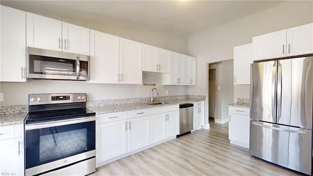 kitchen featuring appliances with stainless steel finishes, white cabinets, a sink, and light stone counters