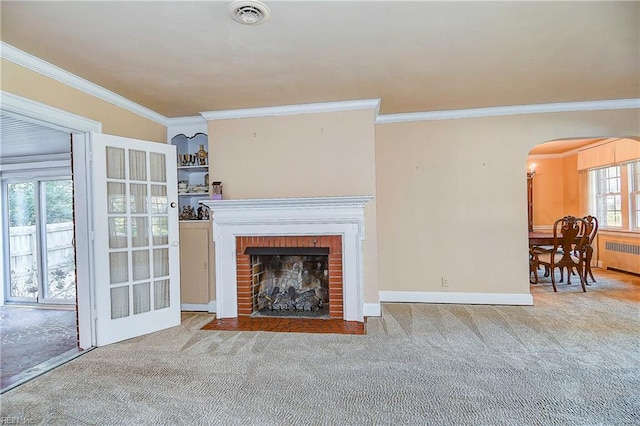 carpeted living room with arched walkways, visible vents, a brick fireplace, radiator heating unit, and crown molding