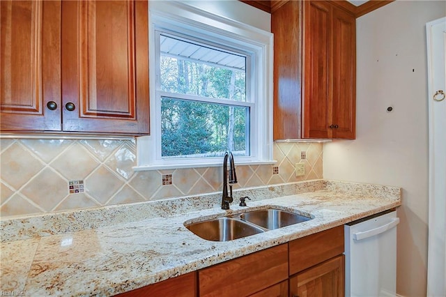 kitchen with dishwasher, brown cabinetry, a sink, and decorative backsplash