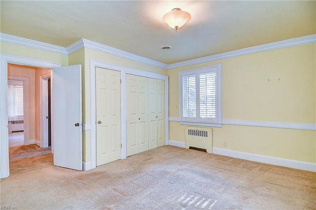 unfurnished bedroom with ornamental molding, carpet, radiator heating unit, and two closets