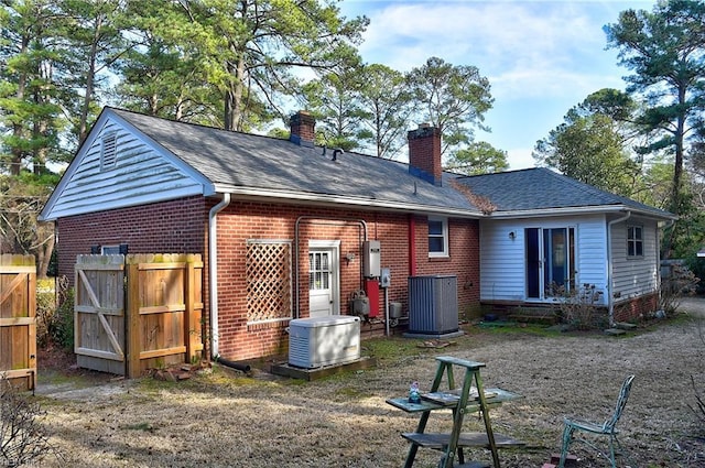 back of house with a shingled roof, cooling unit, brick siding, and a chimney