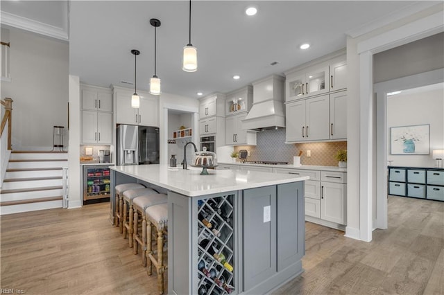 kitchen with wine cooler, a breakfast bar, light countertops, light wood-type flooring, and premium range hood