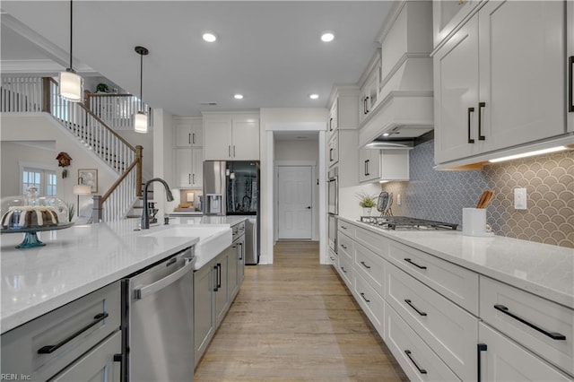 kitchen featuring light stone counters, pendant lighting, stainless steel appliances, light wood-style flooring, and backsplash