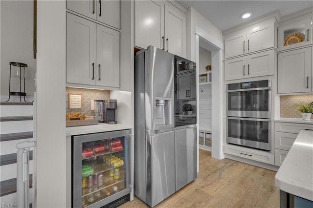 kitchen with light wood finished floors, beverage cooler, decorative backsplash, glass insert cabinets, and appliances with stainless steel finishes