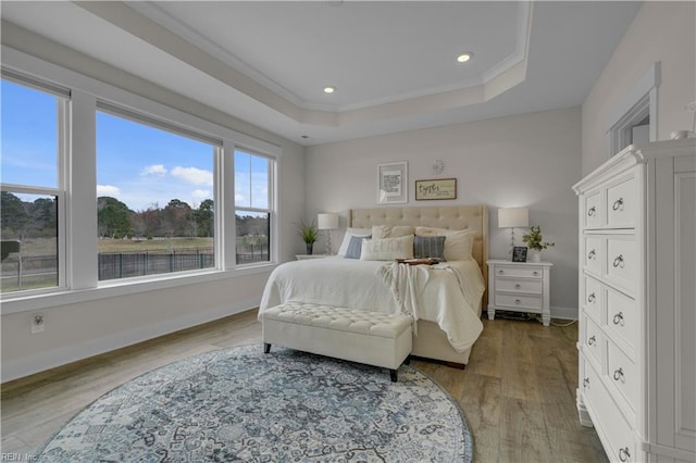 bedroom featuring crown molding, baseboards, a raised ceiling, and wood finished floors