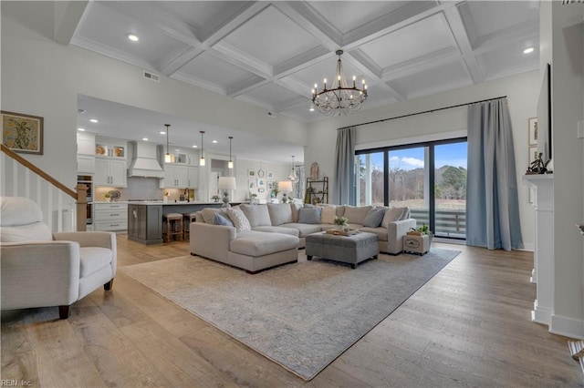 living area featuring coffered ceiling, visible vents, light wood finished floors, beamed ceiling, and an inviting chandelier