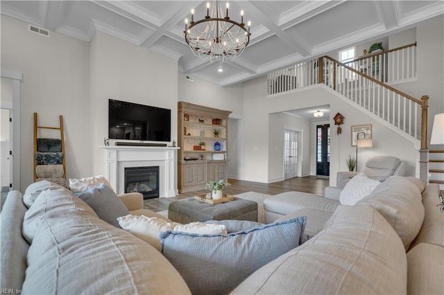 living room featuring visible vents, a towering ceiling, a glass covered fireplace, wood finished floors, and stairs