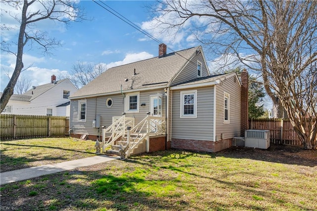 rear view of house featuring a fenced backyard, a yard, a chimney, and roof with shingles