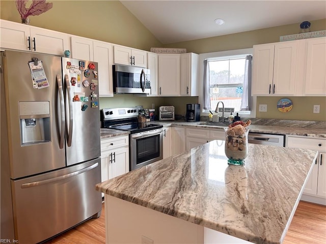 kitchen featuring white cabinets, appliances with stainless steel finishes, a center island, vaulted ceiling, and a sink