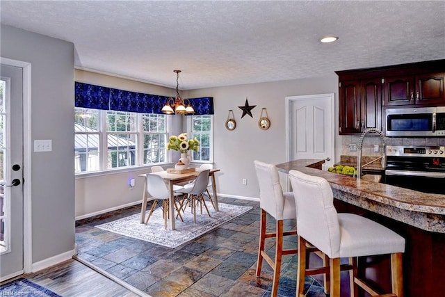 kitchen with a breakfast bar, a notable chandelier, stone tile floors, appliances with stainless steel finishes, and baseboards