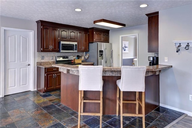 kitchen with a peninsula, baseboards, appliances with stainless steel finishes, and a breakfast bar area