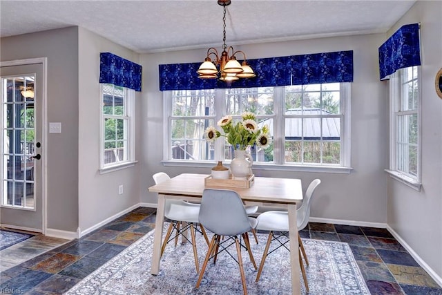 dining space featuring a notable chandelier, a textured ceiling, stone tile flooring, and baseboards