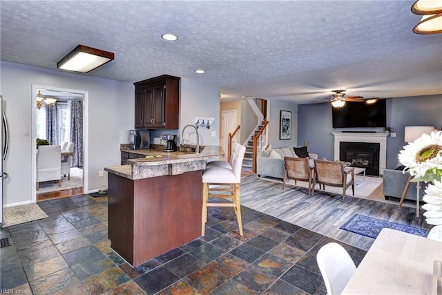 kitchen with a fireplace, a breakfast bar area, recessed lighting, stone tile flooring, and a textured ceiling