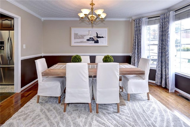 dining room with visible vents, baseboards, wood finished floors, an inviting chandelier, and crown molding