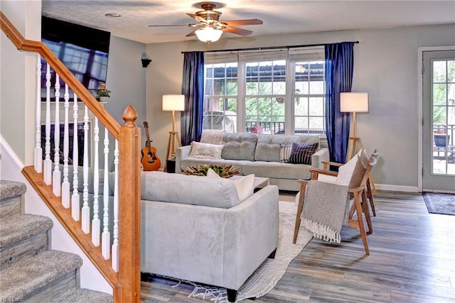 living area with stairs, wood finished floors, a ceiling fan, and baseboards