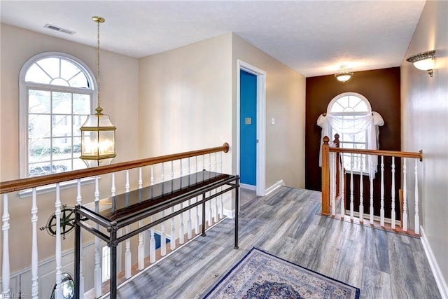 hallway featuring a wealth of natural light, visible vents, an upstairs landing, and wood finished floors