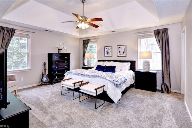 bedroom with light carpet, multiple windows, a raised ceiling, and baseboards