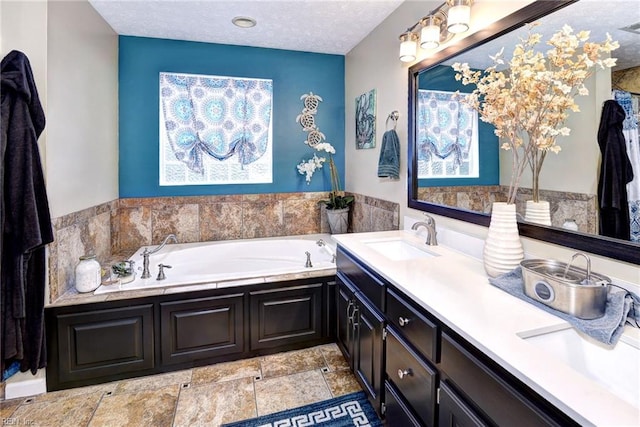 full bathroom featuring a garden tub, double vanity, stone finish floor, a sink, and a textured ceiling