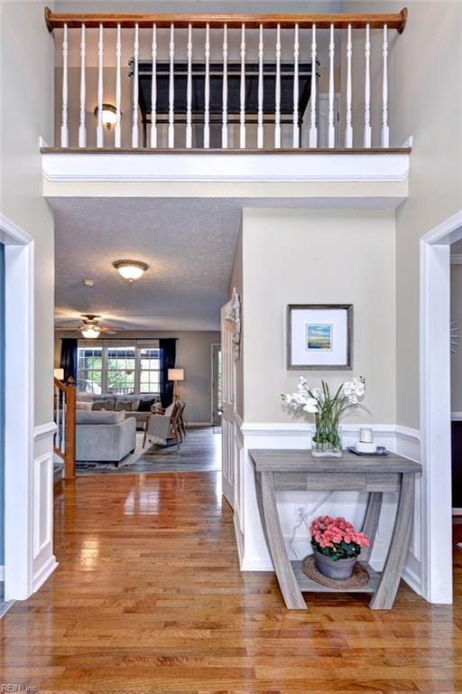 hall with a towering ceiling, a textured ceiling, a decorative wall, and wood finished floors