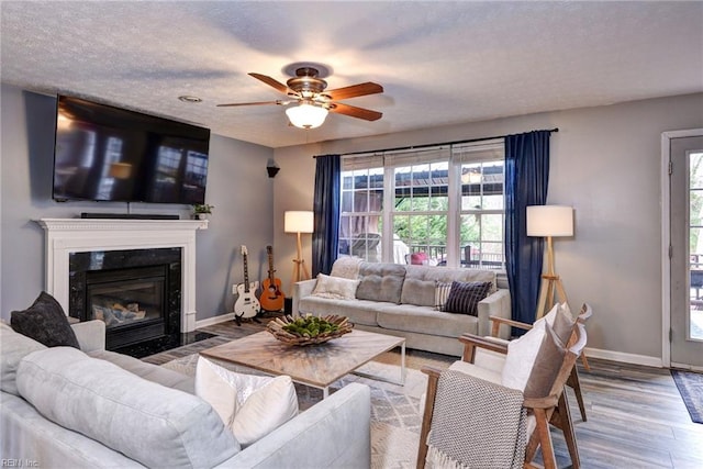 living area featuring a healthy amount of sunlight, a textured ceiling, wood finished floors, and a high end fireplace