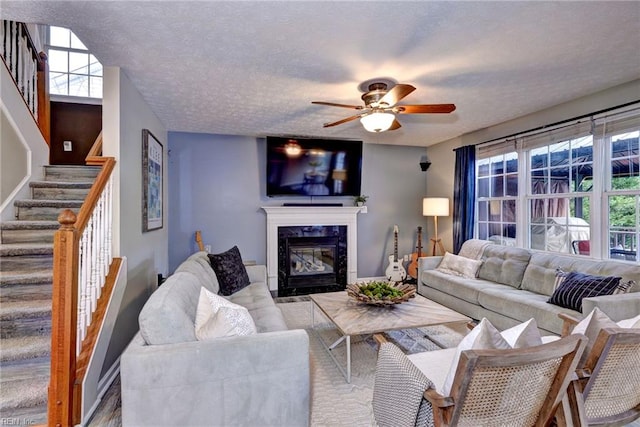 living room with a textured ceiling, stairway, a fireplace, and a ceiling fan