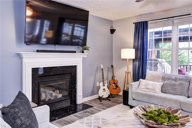 living room with a fireplace, ceiling fan, a textured ceiling, wood finished floors, and baseboards