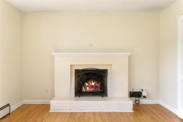 room details featuring baseboard heating, a brick fireplace, wood finished floors, and baseboards