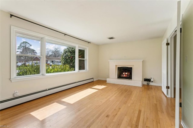 unfurnished living room featuring visible vents, a baseboard heating unit, light wood-type flooring, a lit fireplace, and baseboards