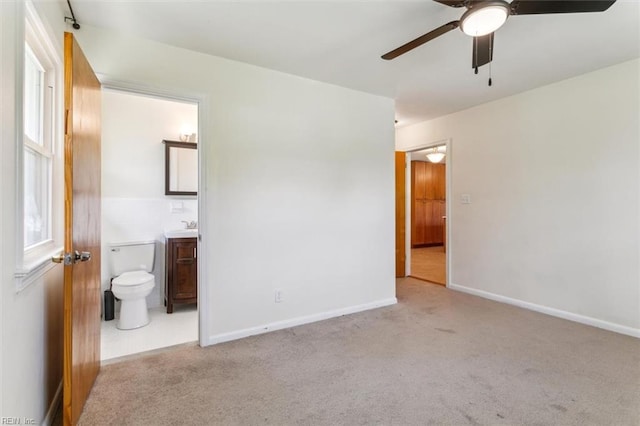 unfurnished bedroom featuring ensuite bathroom, carpet, a ceiling fan, and baseboards