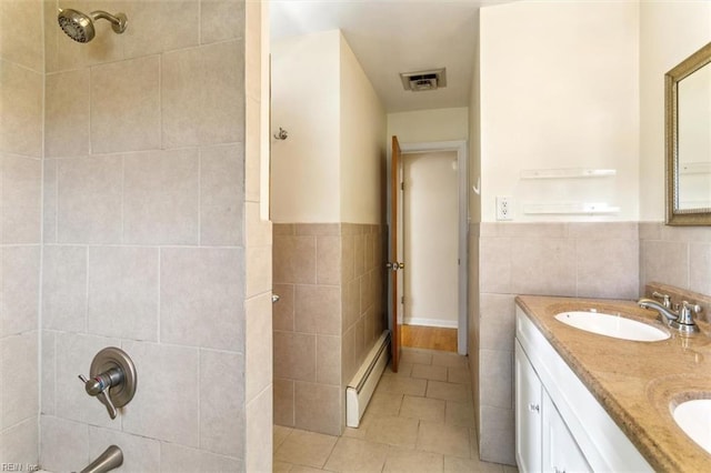 bathroom with double vanity, visible vents, a sink, baseboard heating, and tile walls