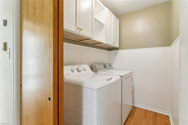 laundry area with light wood-type flooring, cabinet space, a wainscoted wall, and independent washer and dryer