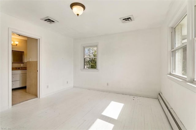 empty room featuring visible vents, baseboard heating, and wood finished floors