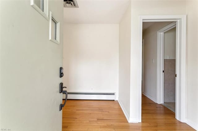 hall with light wood-style flooring, visible vents, a baseboard heating unit, and baseboards