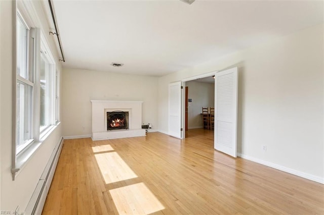 unfurnished living room with light wood finished floors, visible vents, a baseboard heating unit, a brick fireplace, and baseboards