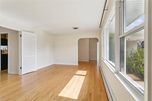 unfurnished room featuring light wood-type flooring, baseboards, visible vents, and arched walkways