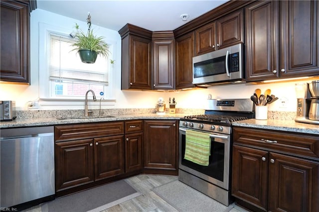 kitchen featuring appliances with stainless steel finishes, a sink, light stone counters, and dark brown cabinets