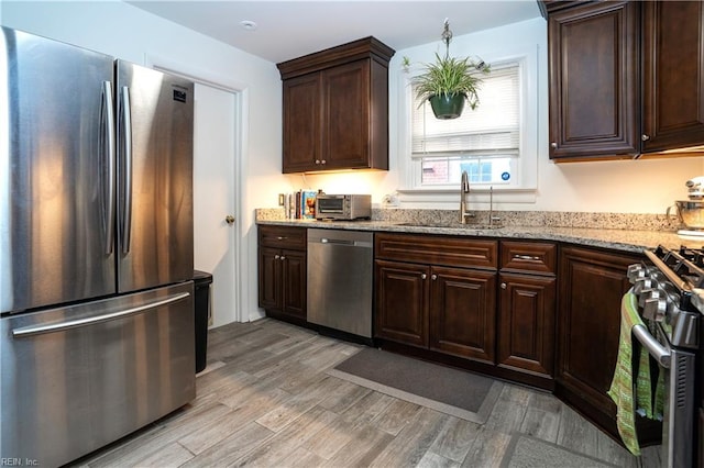 kitchen with a toaster, a sink, dark brown cabinets, appliances with stainless steel finishes, and light wood finished floors