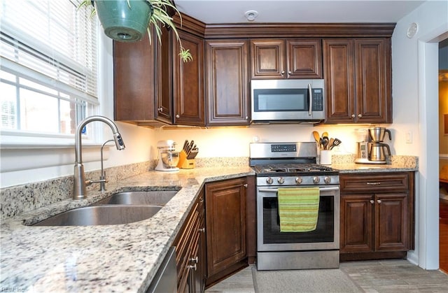 kitchen with stainless steel appliances, light stone counters, a sink, and dark brown cabinets