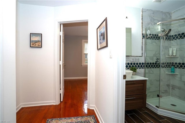 full bath featuring vanity, a shower stall, baseboards, and wood finished floors