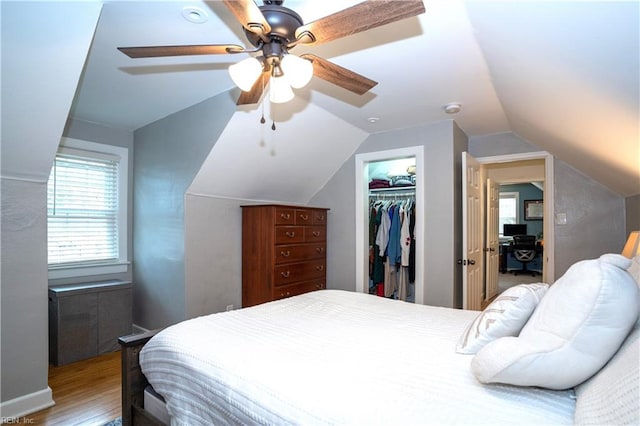 bedroom with ceiling fan, wood finished floors, vaulted ceiling, a spacious closet, and a closet