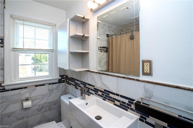 full bath featuring toilet, a wainscoted wall, a shower with shower curtain, a sink, and tile walls