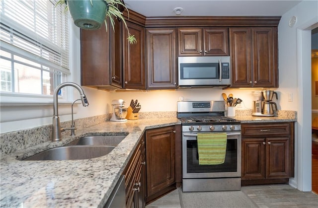 kitchen with appliances with stainless steel finishes, a sink, dark brown cabinetry, and light stone countertops