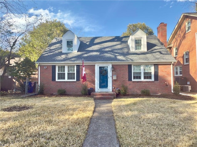 new england style home featuring brick siding, a front lawn, and fence