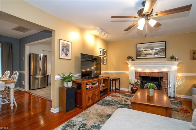 living area with a fireplace, visible vents, ceiling fan, wood finished floors, and baseboards