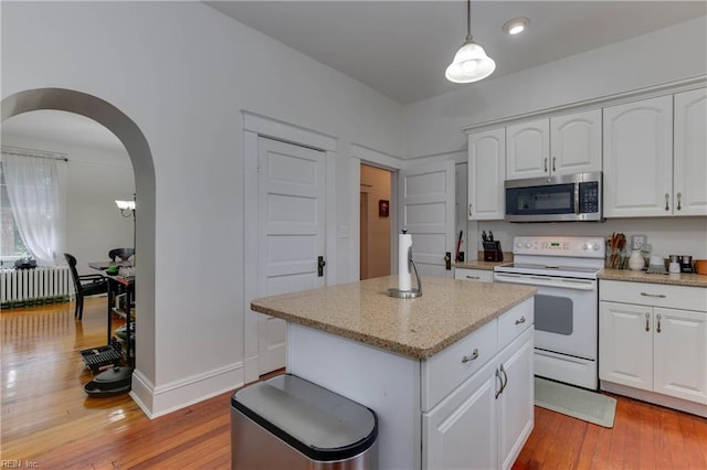 kitchen featuring white range with electric stovetop, arched walkways, stainless steel microwave, a center island, and light wood-style floors