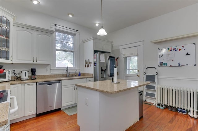 kitchen with stainless steel appliances, a sink, light wood finished floors, radiator heating unit, and plenty of natural light