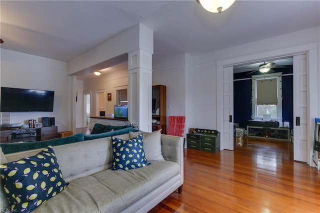 living area with a ceiling fan, light wood-type flooring, and ornate columns