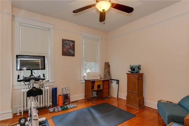 workout area with radiator, wood finished floors, a ceiling fan, and baseboards