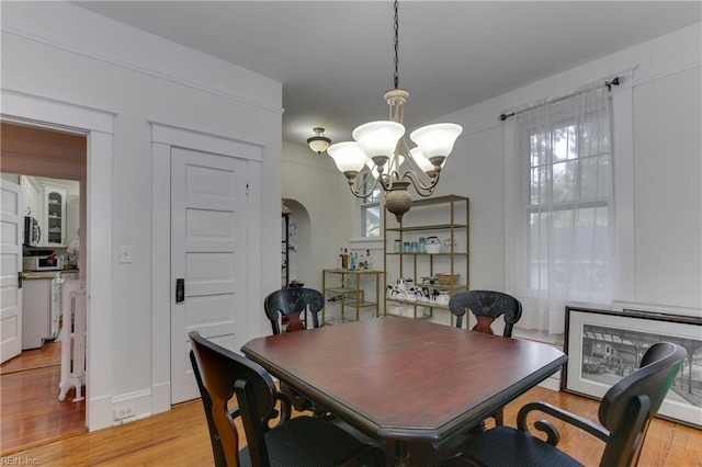 dining room featuring arched walkways, light wood-style flooring, and a notable chandelier